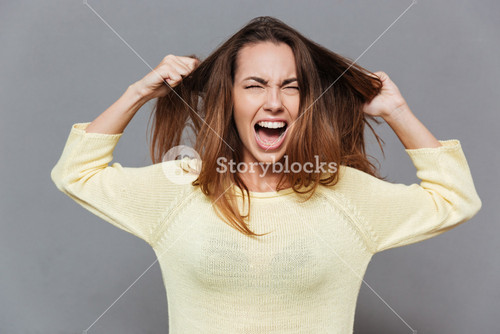 Portrait Of A Frustrated Angry Woman Screaming Out Loud And Pulling Her Hair Out Isolated On The Gray Background